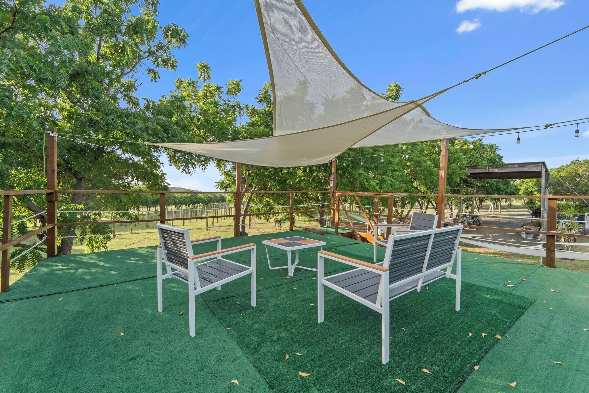 Un área de estar al aire libre con toldo, césped artificial verde y mobiliario de madera.