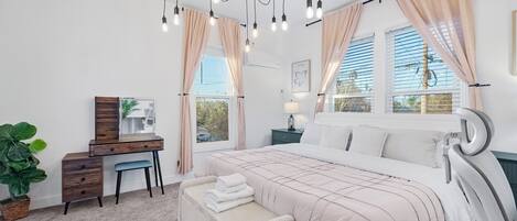 Een slaapkamer met een bed, nachtkastje, lamp, dressoir en gordijnen.