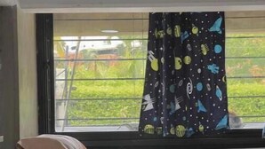 Un lit avec des oreillers, une fenêtre donnant sur un paysage verdoyant et un rideau orné d’un motif sur le thème de l’espace.