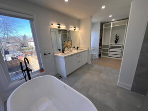 A modern bathroom with a freestanding bathtub, a double vanity with a large mirror, and a walk-in closet.