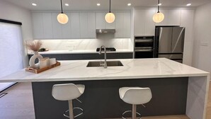 A modern kitchen with a large island, two pendant lights, and a stainless steel refrigerator. - Lakeside Gem - Frenchman's Bay (Pickering)