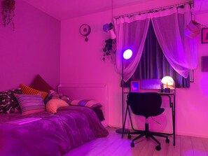 Een slaapkamer met een bed, een bureau met stoel, een computer en een raam met gordijnen.