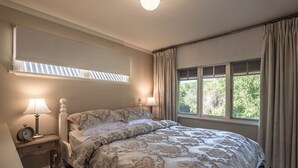 A bedroom with a bed, two bedside tables with lamps, a window with curtains, and a skylight.