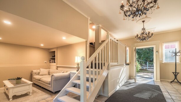 A spacious living room with a white staircase, a chandelier, and a view of the outdoors.