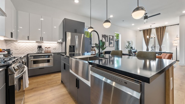 A modern kitchen with stainless steel appliances, a central island, pendant lighting, and a dining area with a sofa and curtains. - Elegant 3BR Stay  2.5 Baths Soothing Hot Tub (Houston)