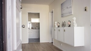 A hallway leading to a kitchen with white cabinets and a decorative shelf with figurines.