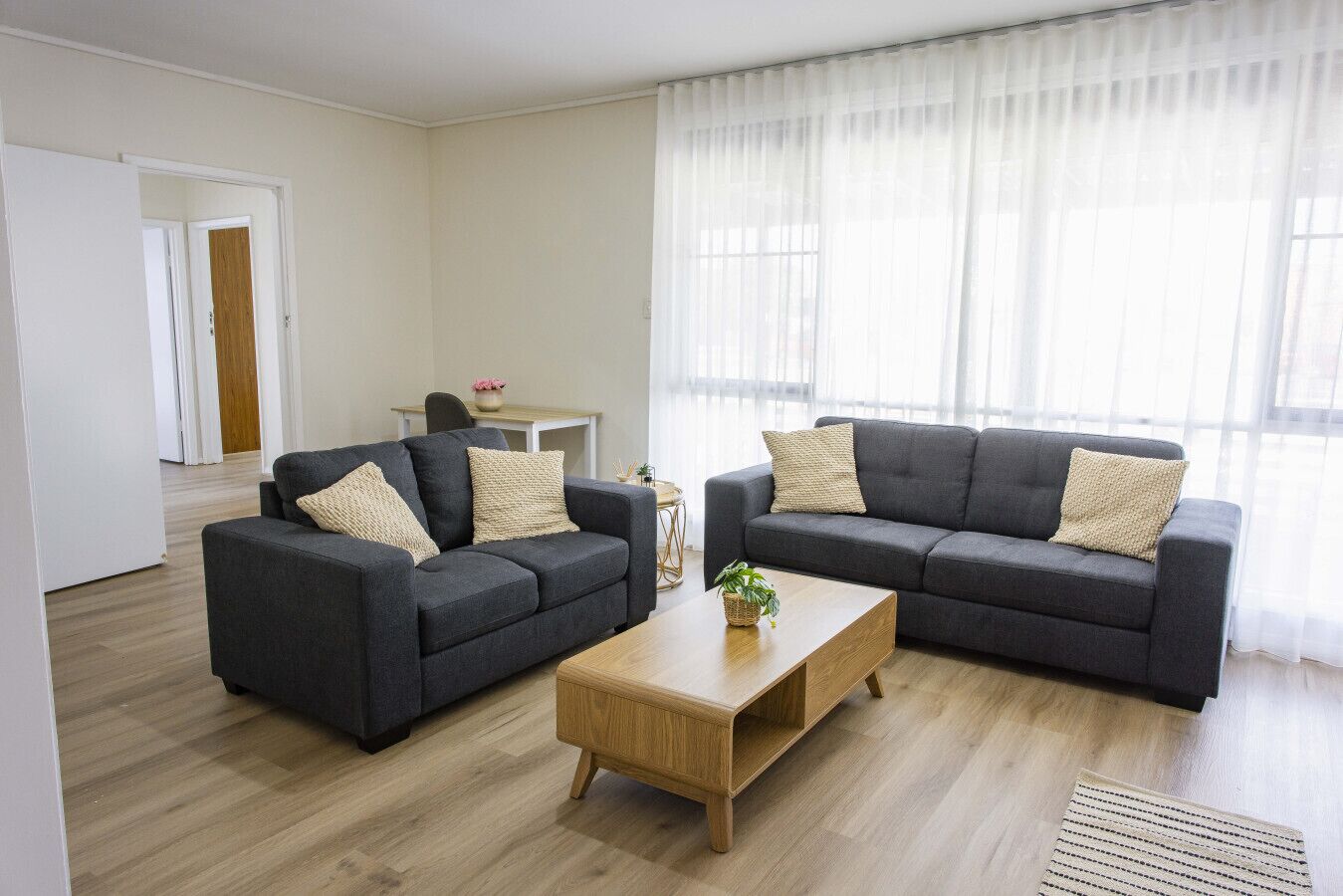 Un salon moderne avec deux canapés gris foncé, une table basse en bois et une petite table d’appoint sur laquelle est posée une plante.