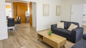 A modern living room with a grey sofa, wooden coffee table, and a dining area with a glass table and chairs.