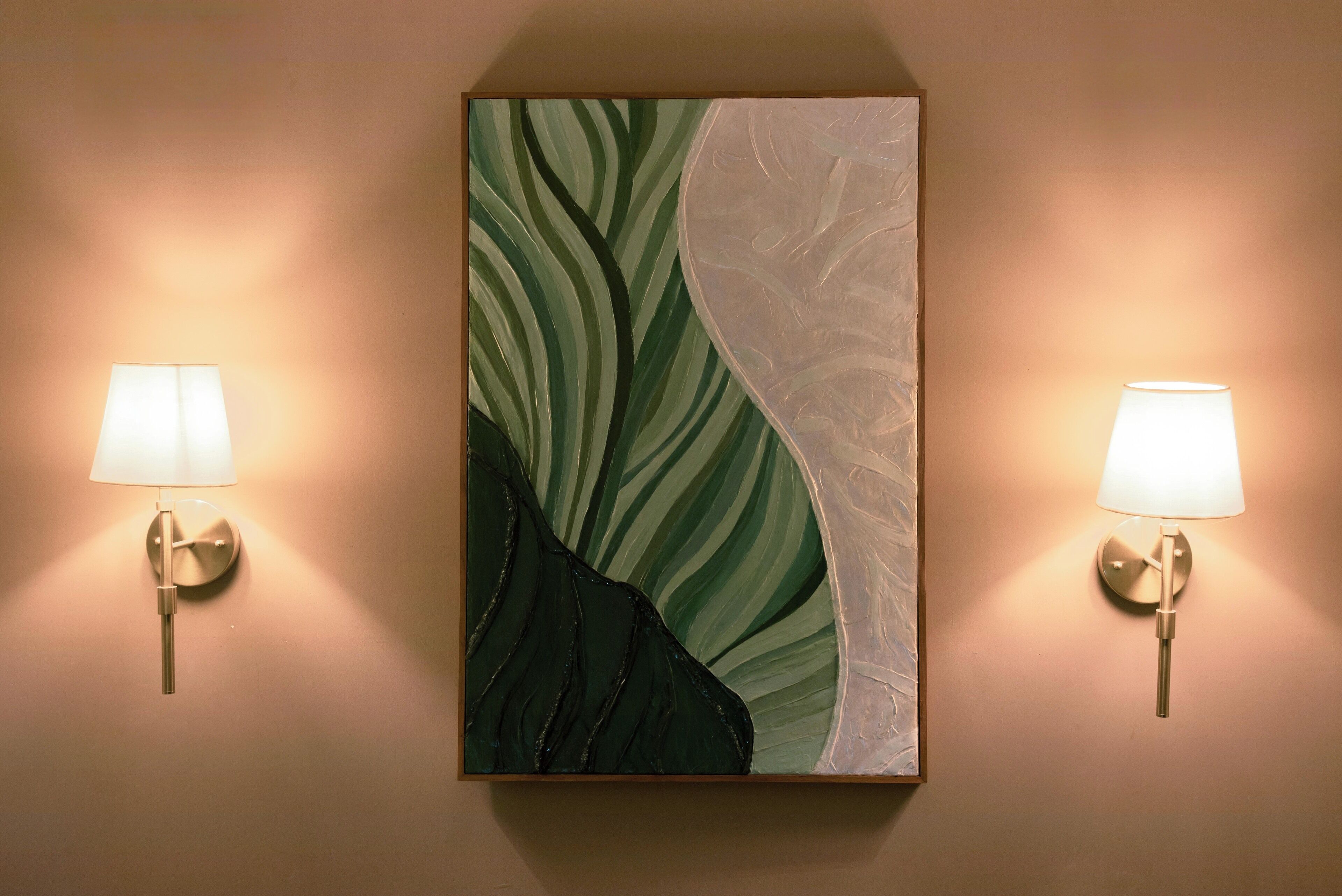 Un tableau mural aux motifs abstraits verts et blancs, encadré de deux lampes fixées au mur.