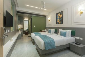 Una habitación de hotel moderna con dos camas, un televisor de pantalla plana, un escritorio y un baño visible a través de una puerta abierta.