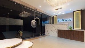 A modern hotel reception area with a marble counter, glass doors, and a chandelier. - The Emerald (Thanjavur)