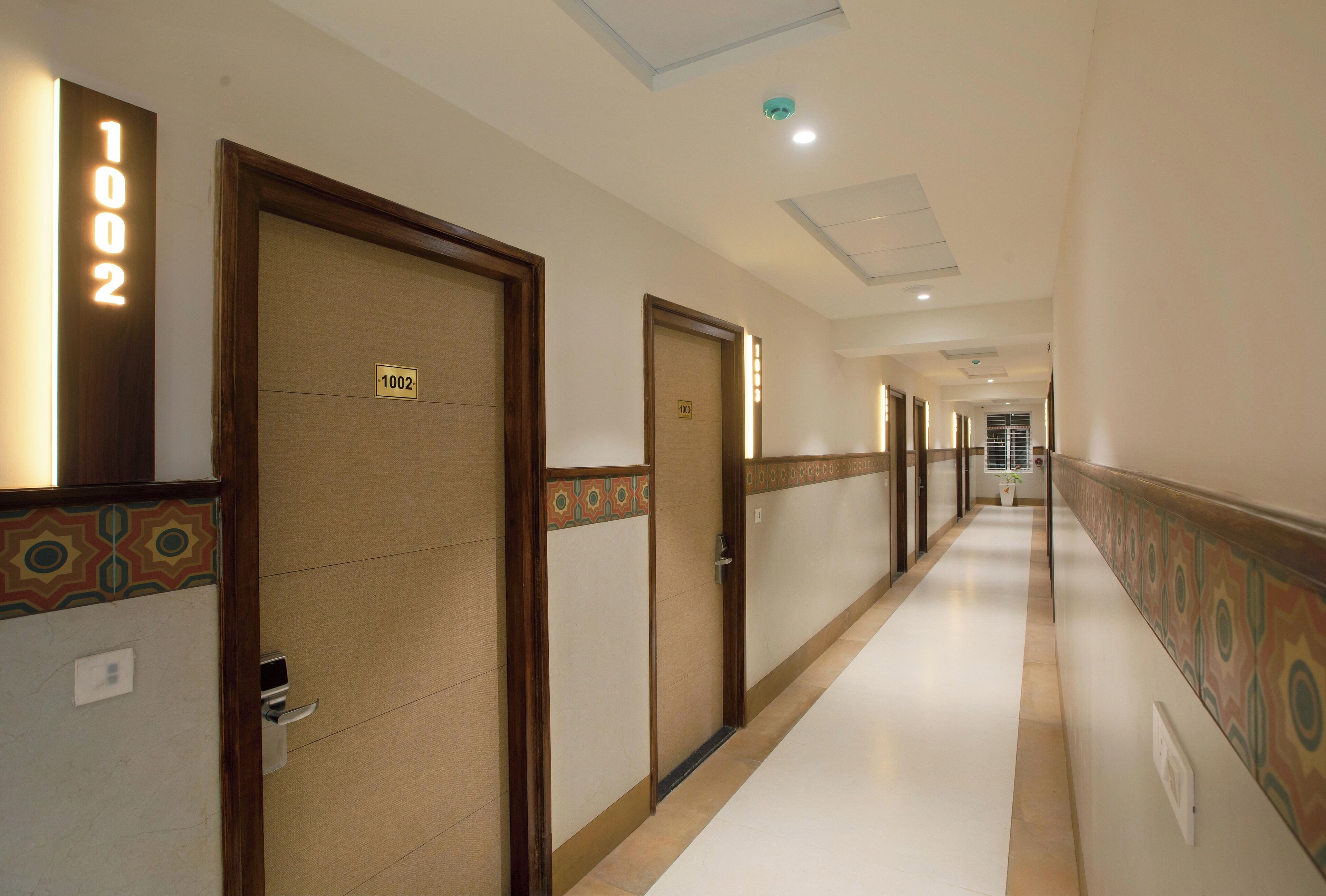 A hotel corridor with doors labeled 1002, a patterned wall design, and a tiled floor.