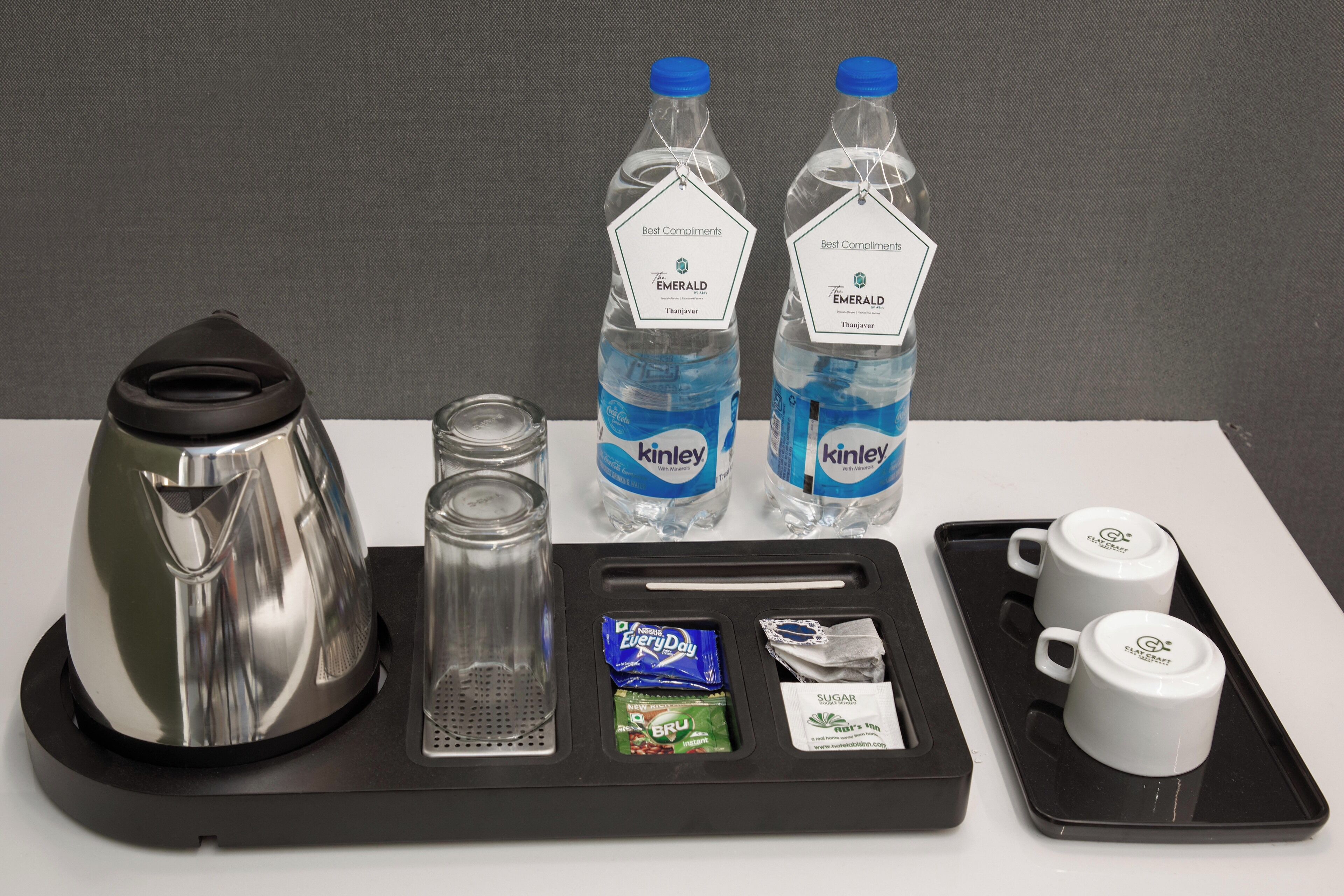 A tray with a kettle, two water bottles, two cups, and some snacks.