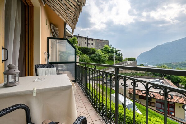 A balcony with a table and chairs, a view of a mountain, and a building in the background. - Studio Apartment 'G and B Apartments Elena' with Mountain View, Shared Pool and Wi-Fi (Tignale sul Garda)