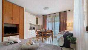 Une chambre d’hôtel comprenant un lit, une télévision, un coin repas et un balcon avec des rideaux.