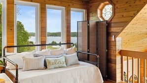 Une chambre aménagée dans une cabane en bois, avec un lit, de grandes fenêtres et une vue sur l’extérieur.