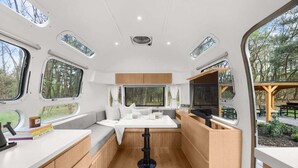 Interior compacto de una autocaravana con kitchenette, zona de estar y ventanas amplias.