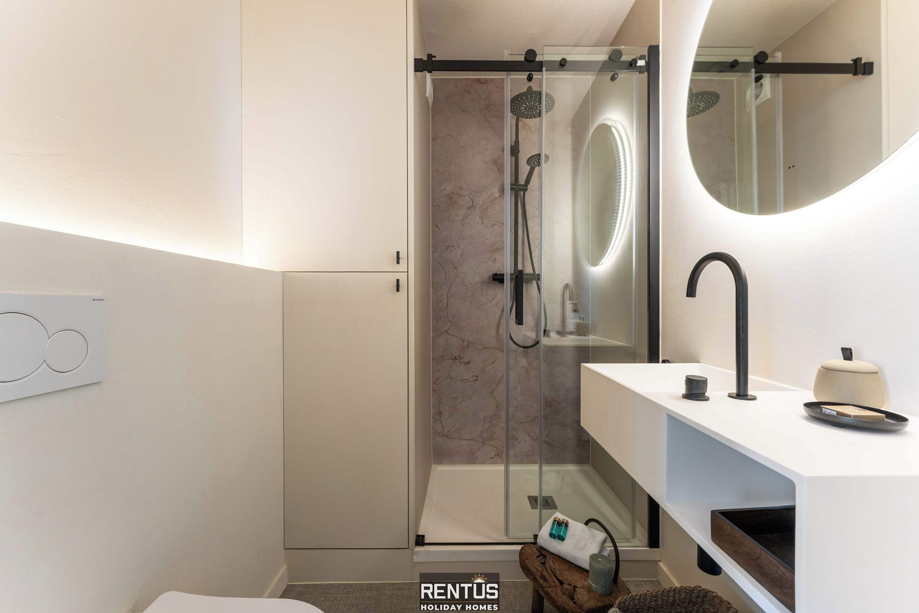 A modern bathroom with a glass shower enclosure, a white vanity with a round mirror, and a minimalist design.