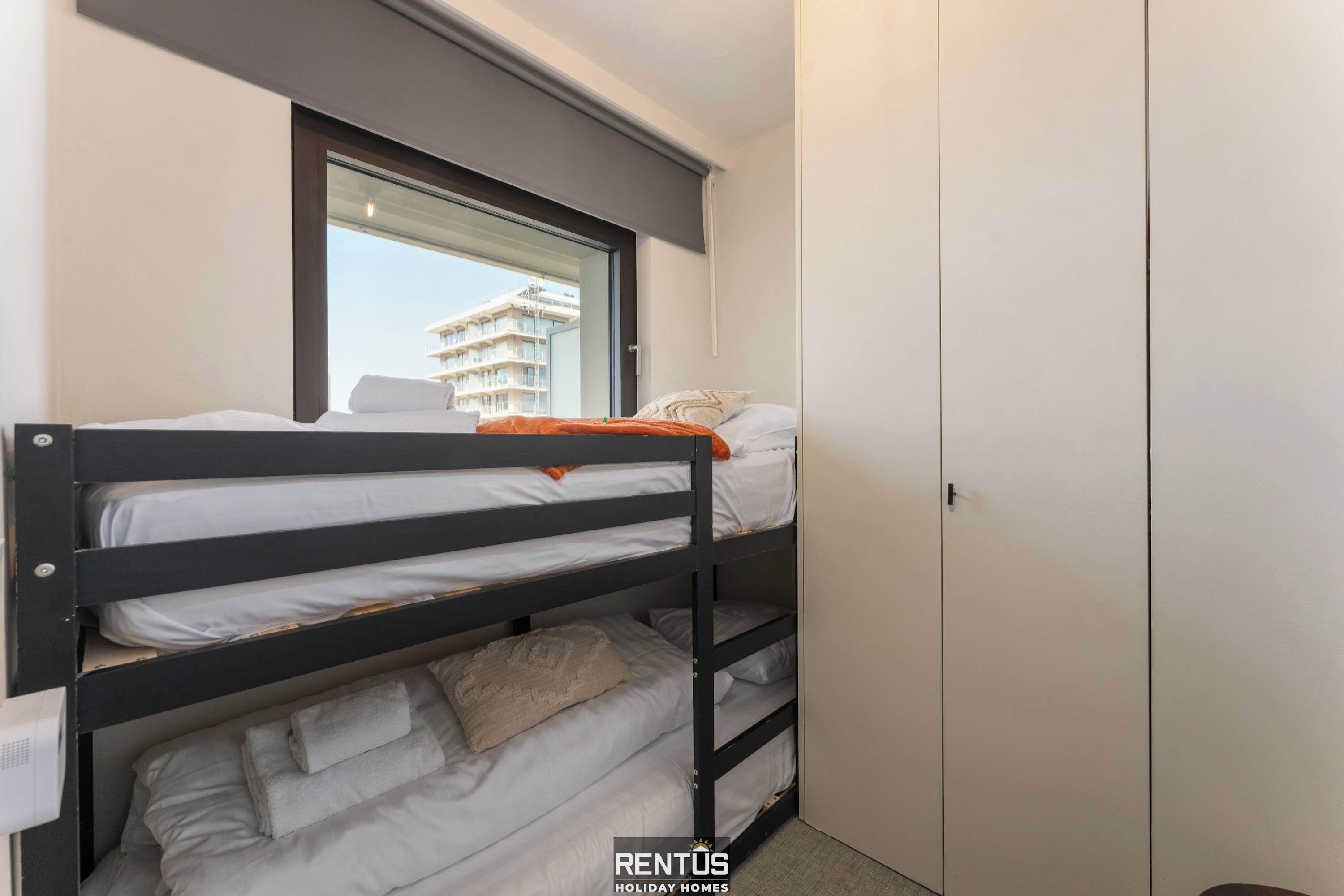 Une chambre avec un lit superposé, une fenêtre, une armoire et un balcon visible.