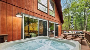 A wooden cabin with a hot tub, sliding glass doors, and a deck with outdoor furniture. - Dog-Friendly Pocono Chalet w/ Hot Tub, Indoor Pool (Long Pond)