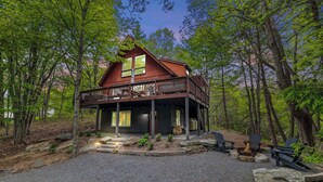 A cabin with a deck, surrounded by trees and a gravel driveway. - Dog-Friendly Pocono Chalet w/ Hot Tub, Indoor Pool (Long Pond)