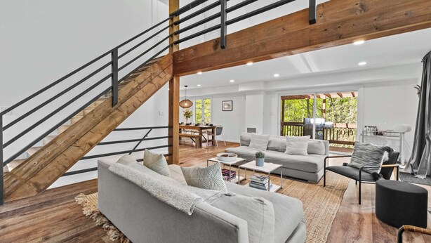 A spacious living area with a staircase, a sofa set, a dining table, and a view of the outdoors. - Dog-Friendly Pocono Chalet w/ Hot Tub, Indoor Pool (Long Pond)
