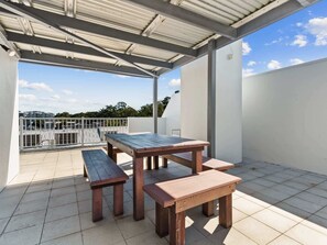 An outdoor patio with a wooden table and benches, a covered area, and a view of the surrounding buildings.