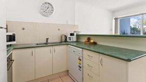 Cocina compacta equipada con microondas, hervidor y un reloj en la pared.