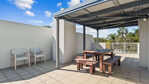 Un patio exterior con un área de estar cubierta, una mesa y dos sillas.