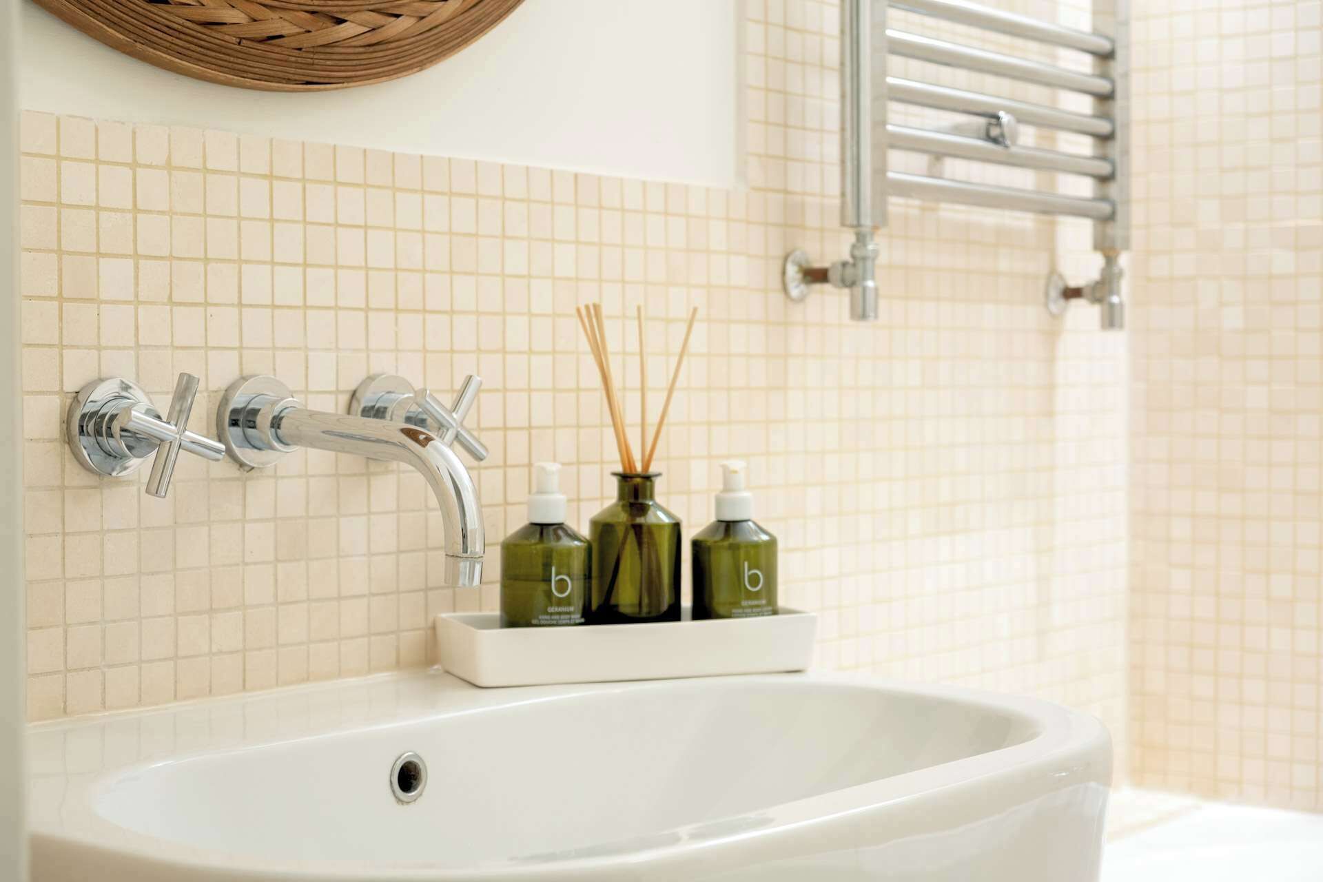 Un baño con lavamanos blanco, grifos cromados, toallero y un difusor de aroma en un frasco.