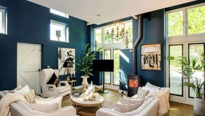A modern living room with a fireplace, comfortable seating, and large windows. - Campden Barn - Luxury Home with Hot Tub (Chipping Campden)