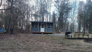Une petite cabane avec une porte d’entrée et des fenêtres, entourée d’une forêt.