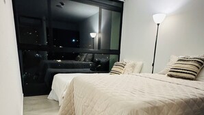 A bedroom with two beds, a large window, and a floor lamp. - Modern Condo - Beautiful City & Volcano Views - 5 min to WTC & Top Places (San Salvador)