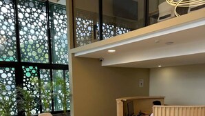 A reception area with a wooden desk, beige sofas, and a large window with a circular pattern. - Modern Condo - Beautiful City & Volcano Views - 5 min to WTC & Top Places (San Salvador)