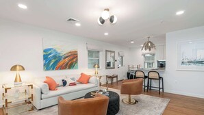 A modern living room with a sofa, ottoman, and chairs, a dining area with a table and chairs, and artwork on the walls. - Beautiful 3 Bedroom Retreat walking distance to Downtown St. Michaels (Saint Michaels)