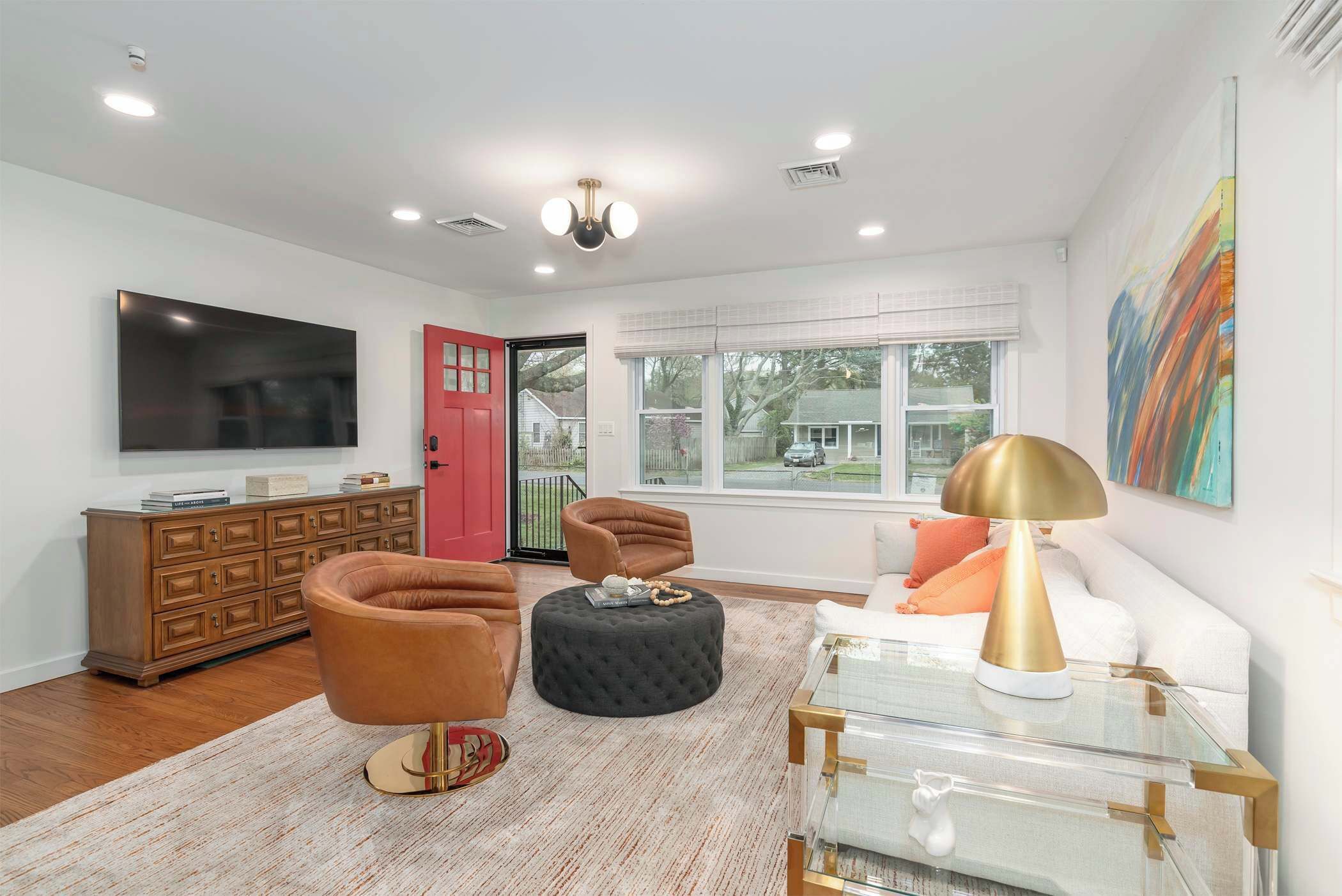Un salon moderne doté d’un téléviseur à écran plat, d’un meuble en bois, d’une porte rouge, d’une fenêtre offrant une belle vue et d’un grand tableau abstrait.
