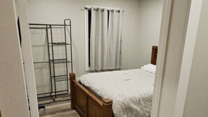 Une chambre avec un lit en bois, des rideaux blancs, un étagère en métal et un plancher en bois.