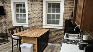 Une cuisine avec un îlot central en bois, deux fenêtres, un évier et une poubelle.