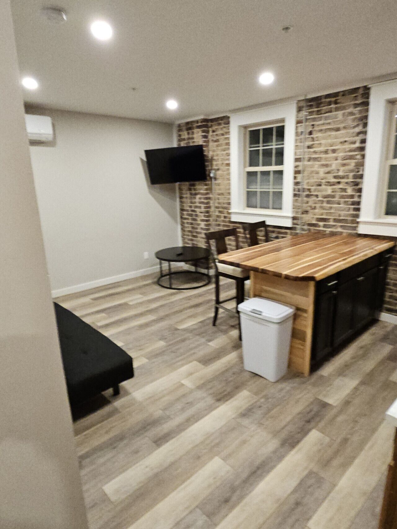 Une cuisine compacte avec un îlot central en bois, une chaise noire, une petite table et un téléviseur fixé au mur.