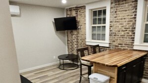 Une cuisine compacte avec un îlot central en bois, une chaise noire, une petite table et un téléviseur fixé au mur.