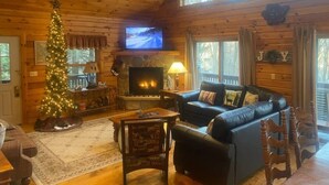 A cozy cabin interior with a fireplace, a television, a Christmas tree, and a leather sofa. - Knotty Dog Lodge- Hot Tub, Fire Pit, Pet Friendly! (Oakland)