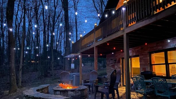 An outdoor patio with a fire pit, seating, and a covered area with string lights. - Knotty Dog Lodge- Hot Tub, Fire Pit, Pet Friendly! (Oakland)