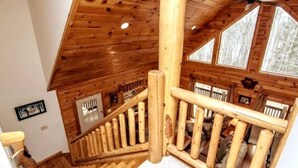 A wooden staircase with a railing, a ceiling fan, and windows with a view of trees. - Knotty Dog Lodge- Hot Tub, Fire Pit, Pet Friendly! (Oakland)