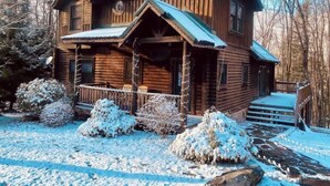 A log cabin with a porch, steps, and snow-covered surroundings. - Knotty Dog Lodge- Hot Tub, Fire Pit, Pet Friendly! (Oakland)