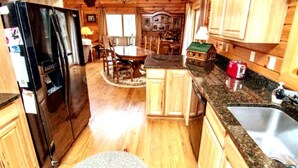 A wooden cabin interior with a kitchen, dining area, and a small living space. - Knotty Dog Lodge- Hot Tub, Fire Pit, Pet Friendly! (Oakland)