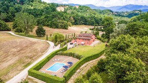 Una casa grande con piscina, rodeada de césped y árboles cuidados.