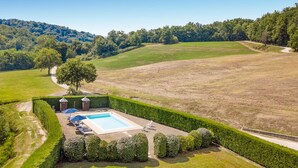 Una piscina rectangular grande con un deck perimetral, rodeada de césped y setos bien cuidados.