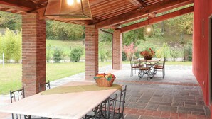 Un patio al aire libre con suelo de ladrillo, una mesa con sillas y una lámpara colgante.