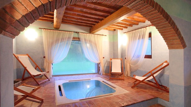 Un cuarto de spa con un jacuzzi, dos sillones de madera y un ventanal con cortinas translúcidas.