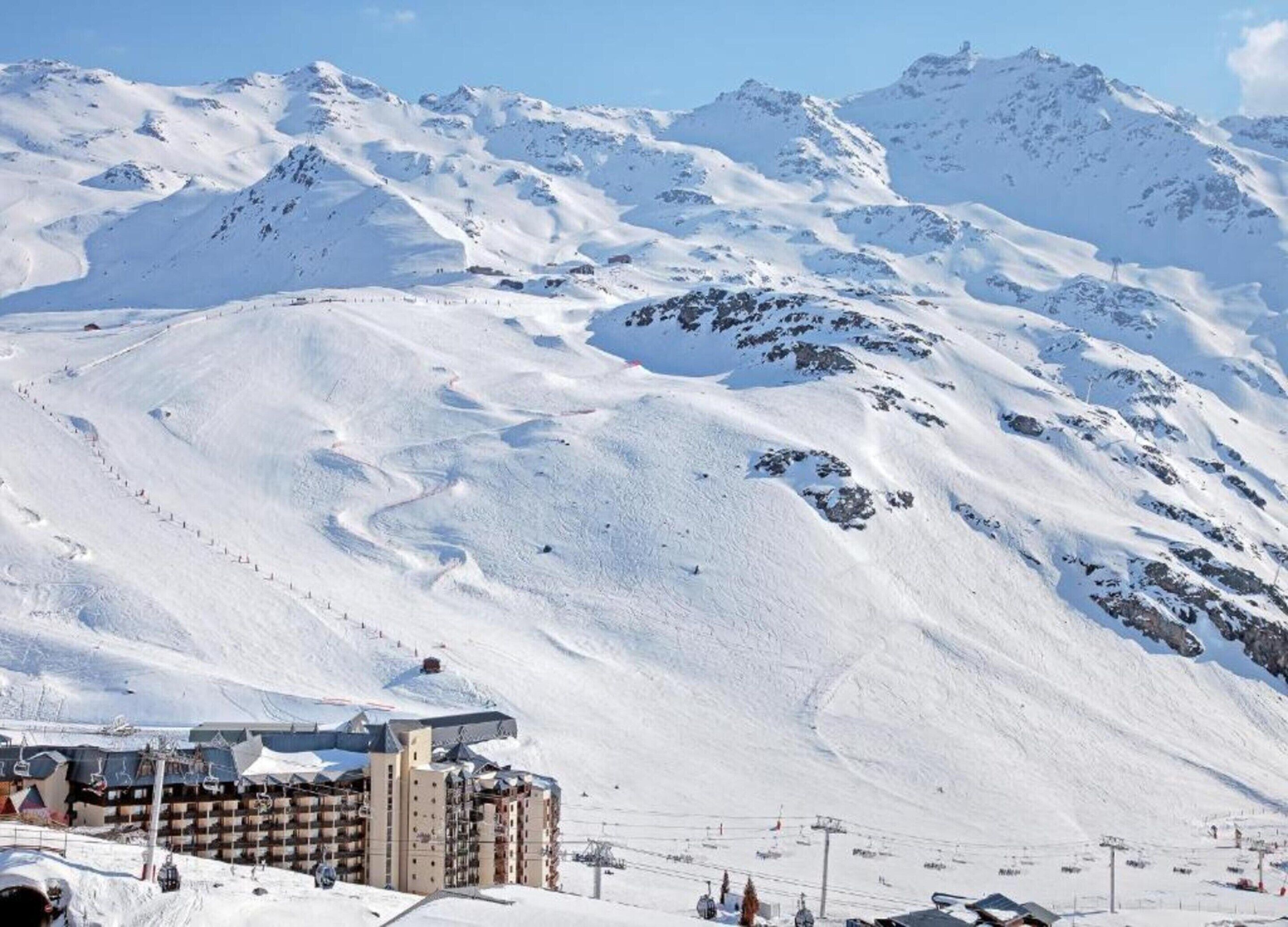 A snow-covered mountain with a ski resort building in the foreground.